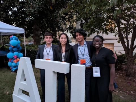 photo of four people standing with behind large white letters