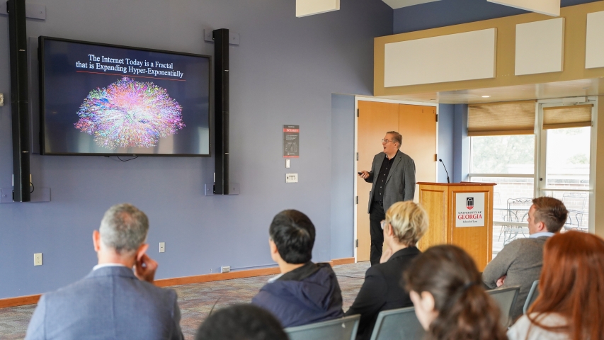 photo of man speaking, with screen, audience
