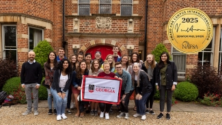 group photo of people in front of old brick building, holding flag