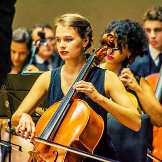 photo of woman playing cello, with other performers in background