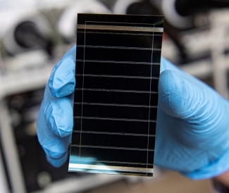 photo of tiny solar cell, held by blue-gloved hand