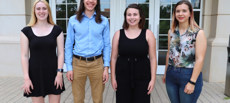Photo of four scholarship awards winners outside in front of a building