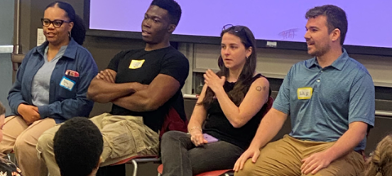 photo of four people seated with name tags, audience