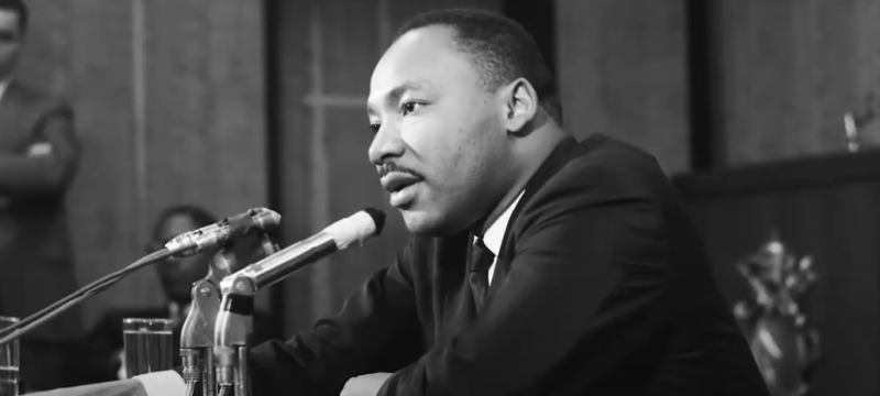 black and white photo of man seated at table with microphone
