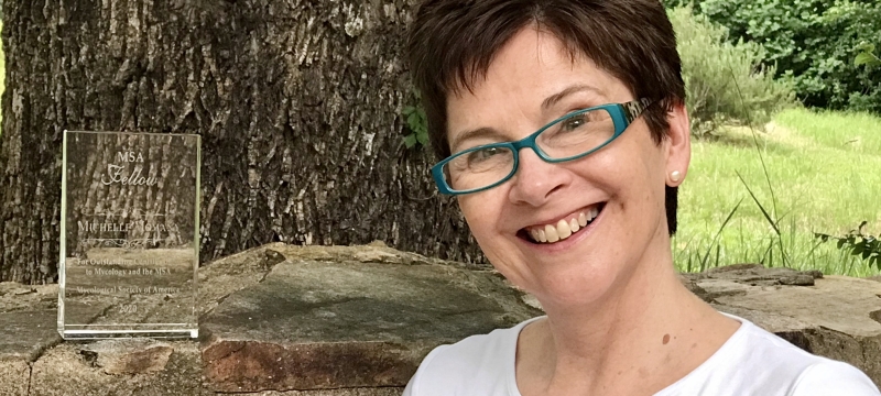 photo of woman outdoors with rock wall and glass plaque