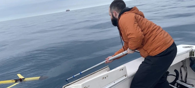 photo of man on boat in ocean with tool reaching for drone in water
