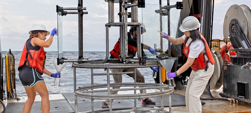 photo of equipment and people on board a ship, sea in background, day