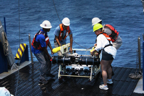 photo off four people with large device in deck of ship, day, water in background