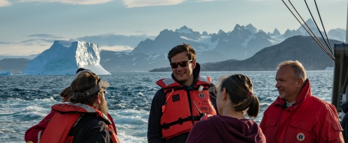 photo of people on ship, mountains in background, day